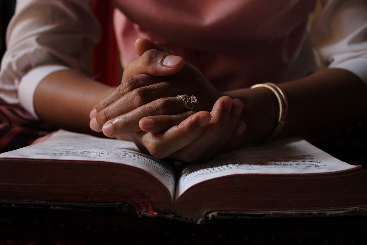 The hands of a black woman praying over the Bible