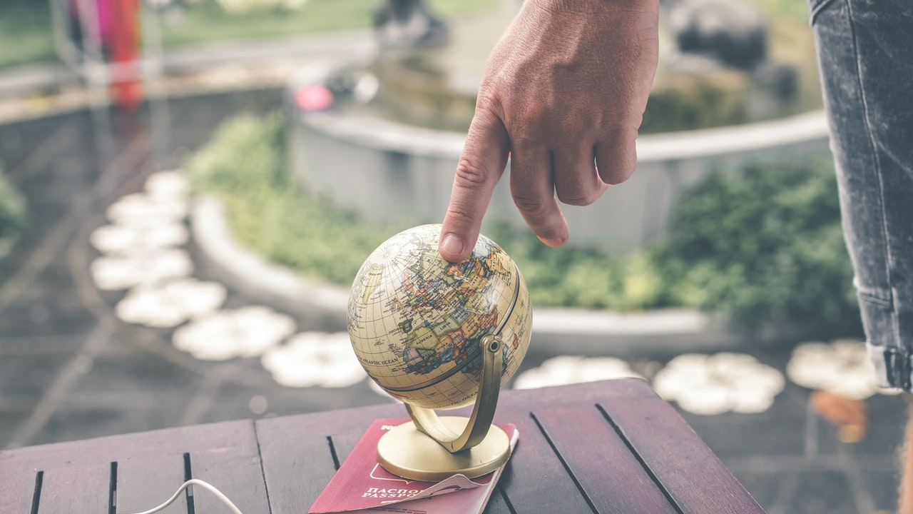 A person's finger pointing to a globe on top of a brown table