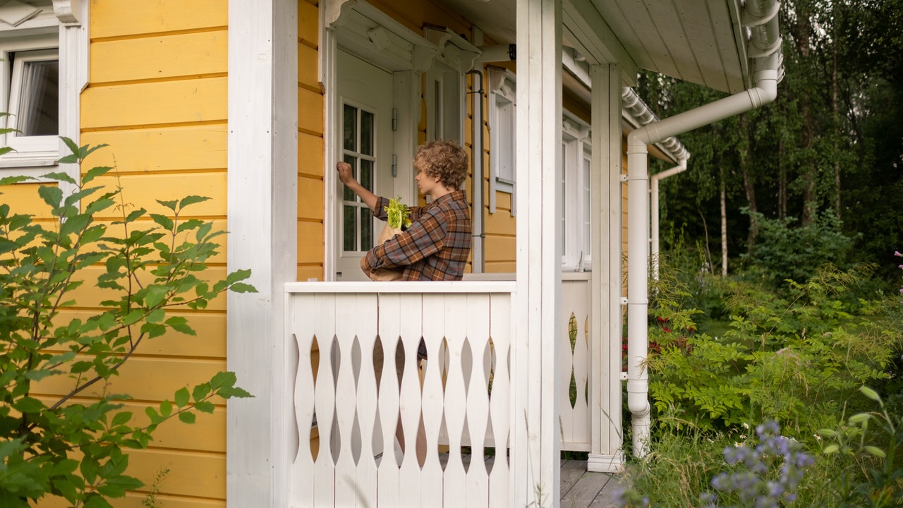 A Teenage boy standing on a porch and knocking on door.