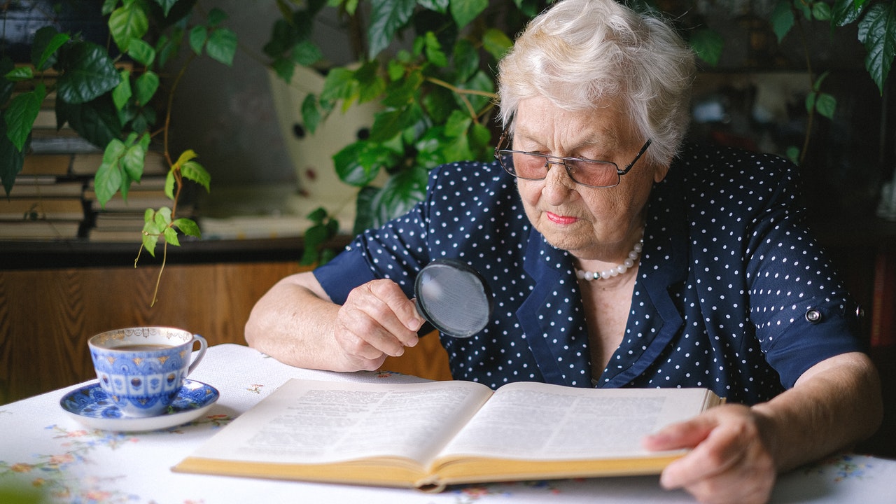 Lovely elderly woman reading a book with magnifiers.
