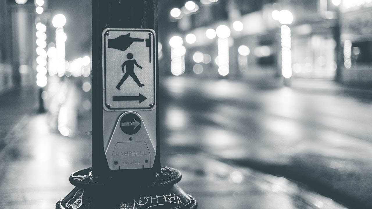 Pedestrian crosswalk button placed near road in city at night time.