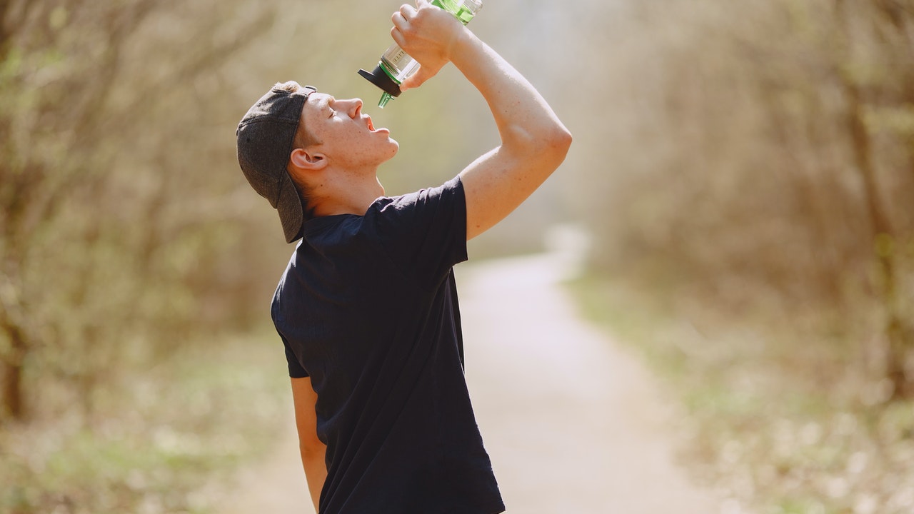 Thirsty man drinking water from a bottle while training in a park.