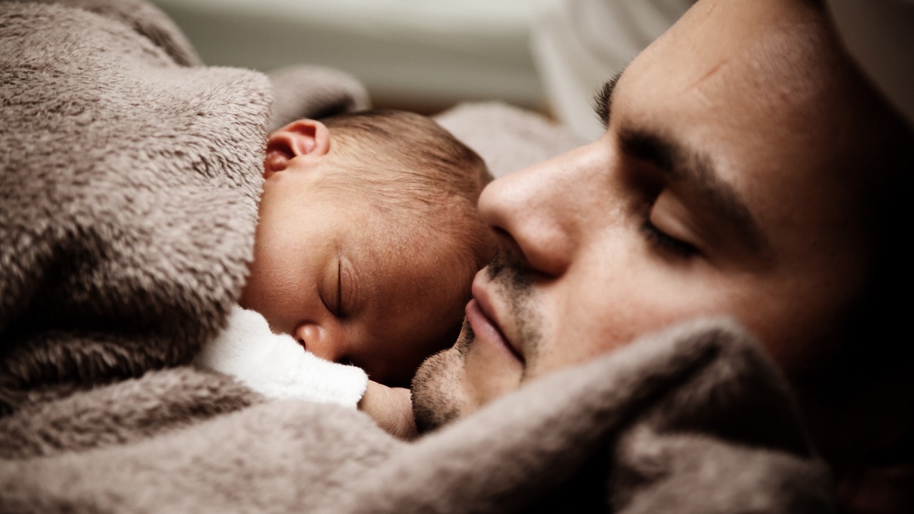A close up of a sleeping man with a sleeping baby on his chest.